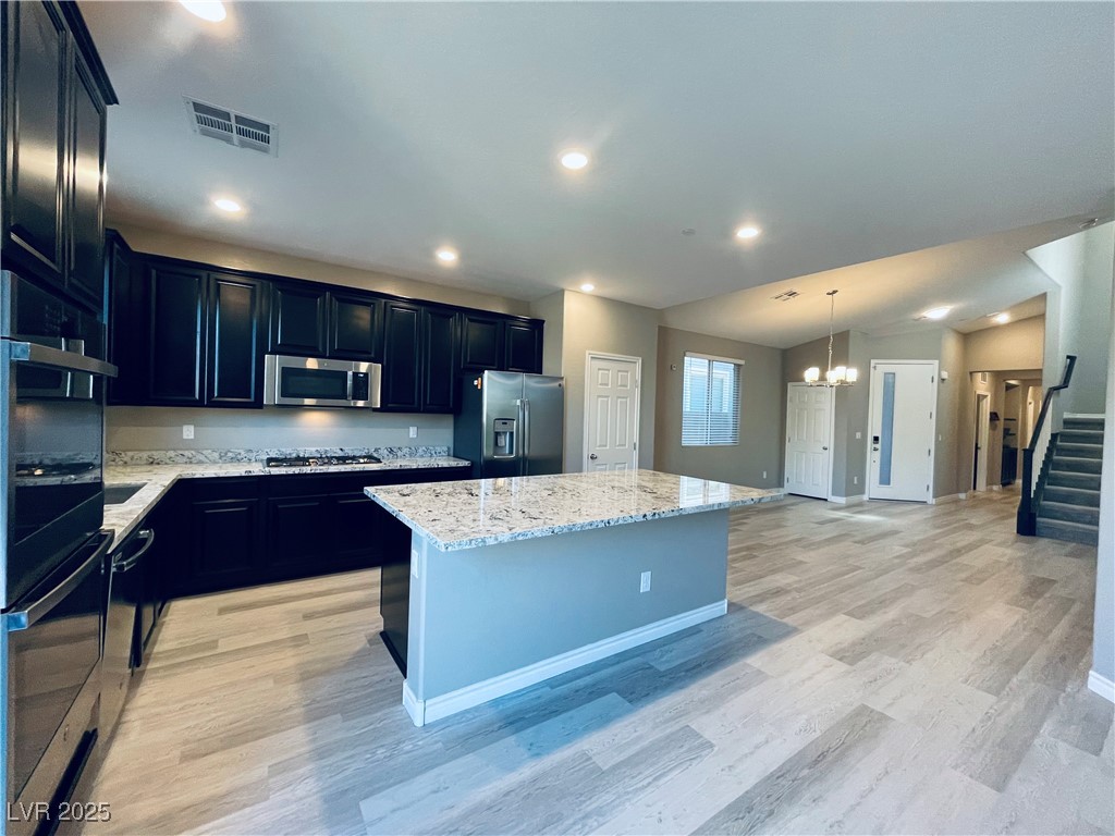 Kitchen featuring dark cabinetry, light stone counters, appliances with stainless steel finishes, light wood-type flooring, and a kitchen island