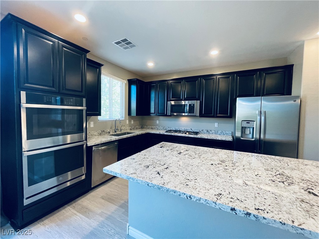 930 Bayberry Ridge Street Henderson, NV 89052 - Photo 11 of 40 Kitchen featuring stainless steel appliances, light stone countertops, light wood-style floors, dark cabinetry, and recessed lighting