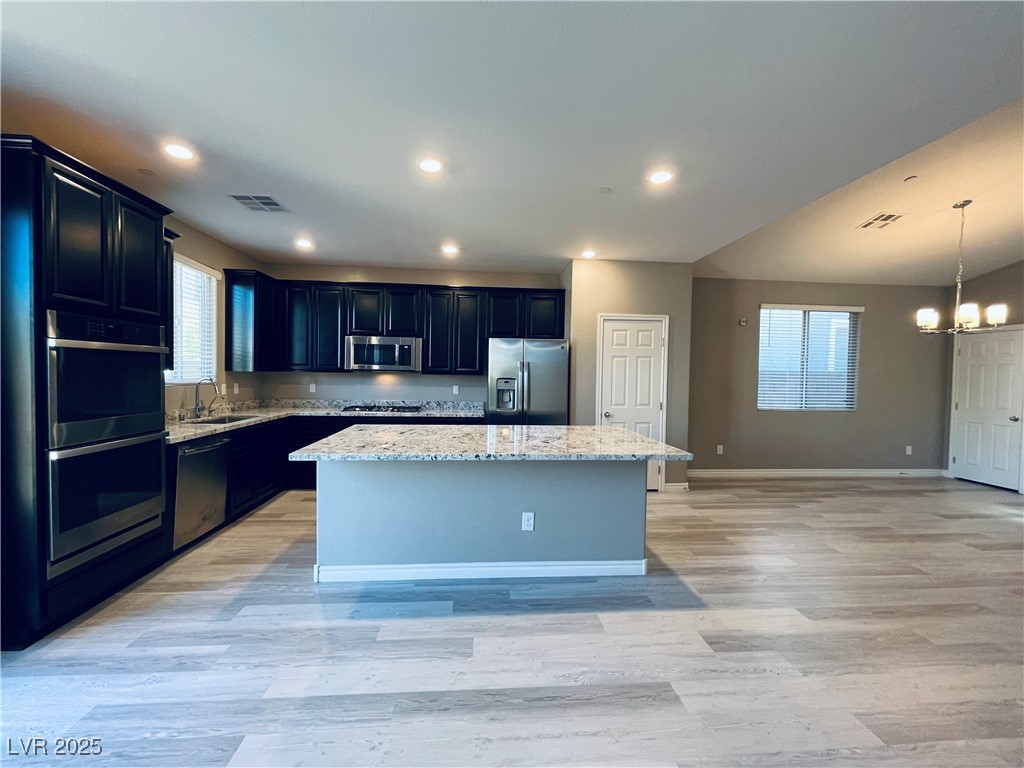 930 Bayberry Ridge Street Henderson, NV 89052 - Photo 9 of 40 Kitchen featuring dark cabinetry, light stone countertops, stainless steel appliances, a center island, and light wood-type flooring
