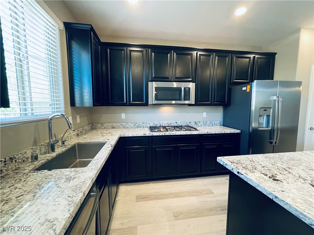 930 Bayberry Ridge Street Henderson, NV 89052 - Photo 10 of 40 Kitchen featuring light stone counters, light wood-style floors, stainless steel appliances, dark cabinetry, and recessed lighting