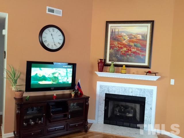 4708 Silverdene Street Raleigh, NC 27616 - Photo 10 of 14 a living room with a fireplace a flat screen tv and a wall clock