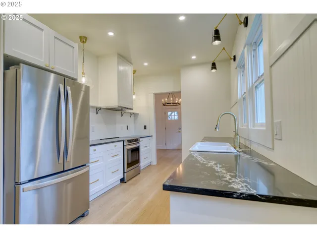 a kitchen with stainless steel appliances granite countertop a refrigerator a sink and white cabinets