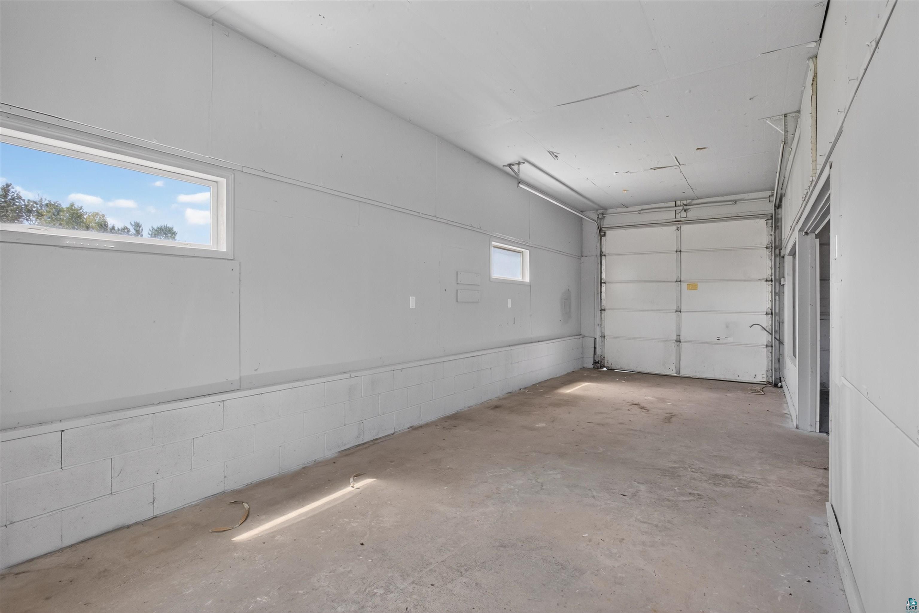 5868 Rice Lake Road Duluth, MN 55803 - Photo 34 of 39 Spacious interior featuring a large roll-up door, concrete flooring, and multiple windows providing natural light