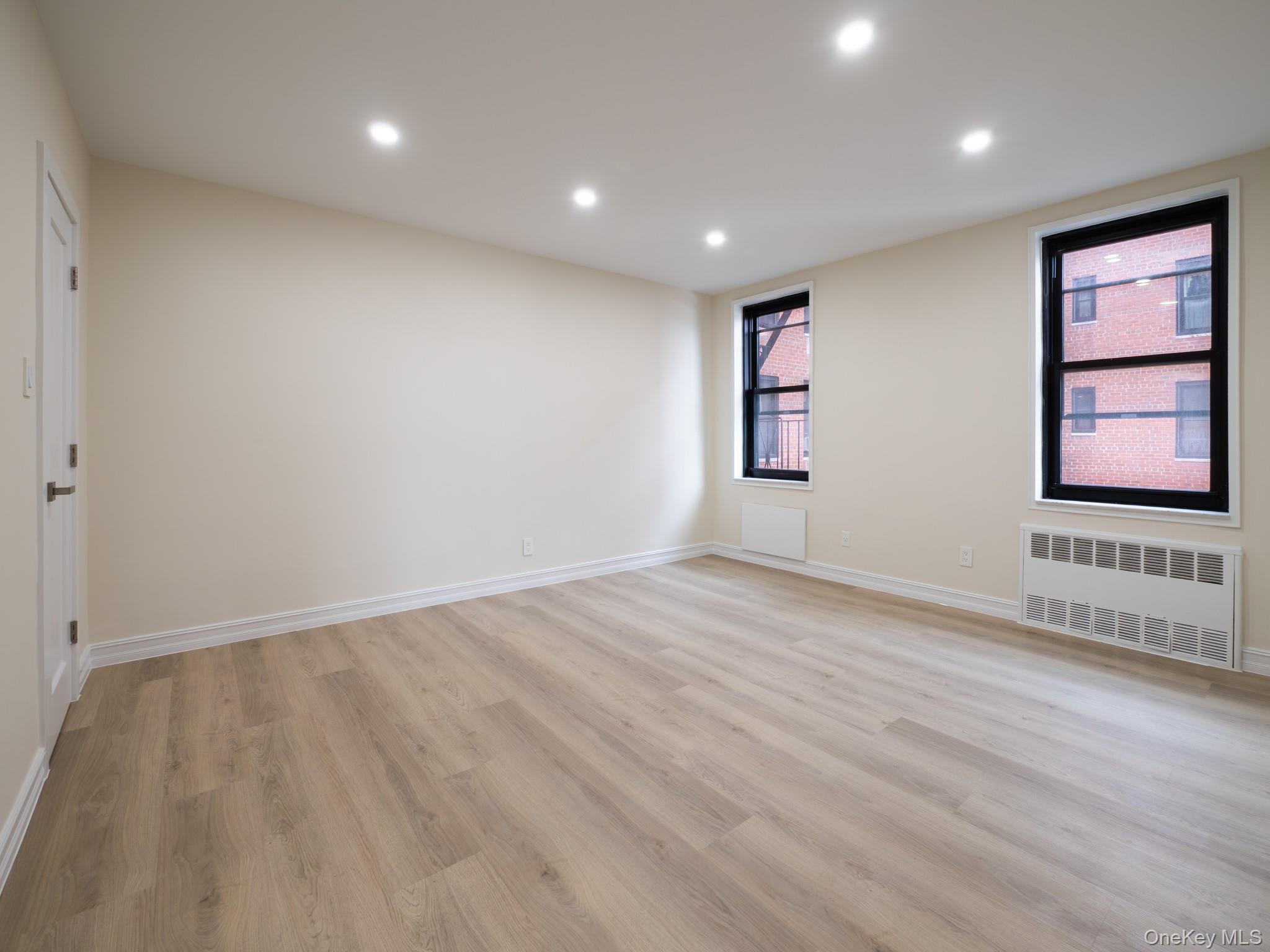 139-15 83rd Avenue, Unit 423 Queens, NY 11435 - Photo 17 of 24 Empty room featuring radiator heating unit, light wood finished floors, and recessed lighting