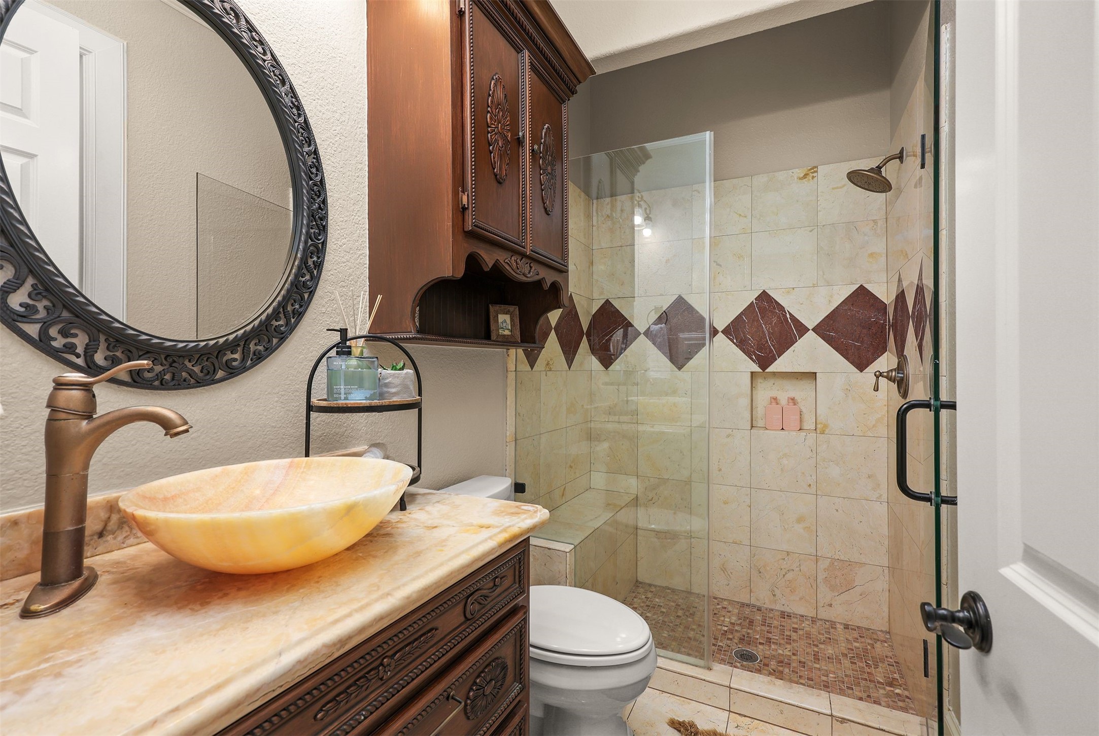 10896 Decatur Street Willis, TX 77318 - Photo 21 of 50 This bathroom exudes luxury with its elegant vessel sink atop a marble countertop, ornate cabinetry, and a glass-enclosed shower featuring exquisite tile work, perfectly blending classic and modern design elements.