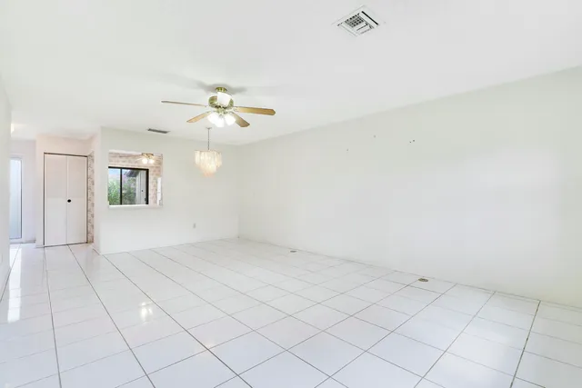 an empty room with chandelier fan and windows