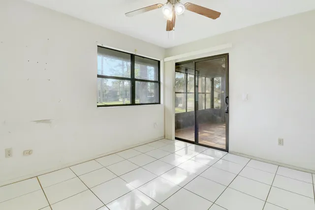 an empty room with chandelier fan and windows