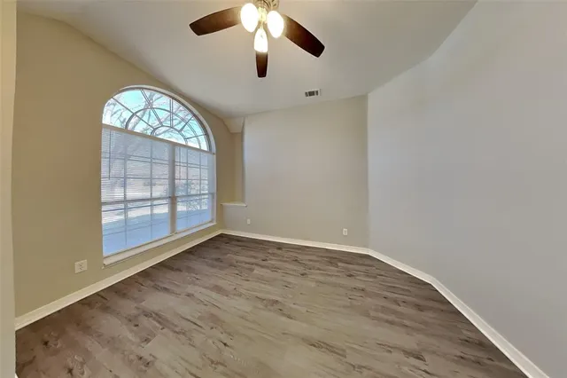 an empty room with wooden floor chandelier fan and windows