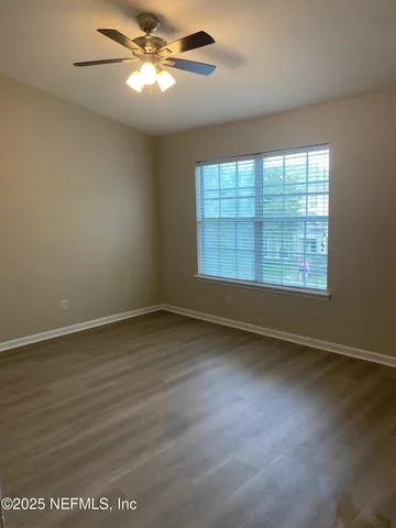 an empty room with wooden floor fan and windows