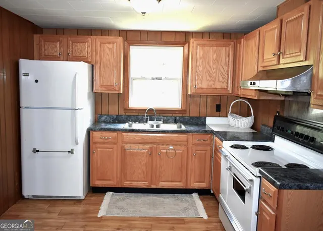 a kitchen with granite countertop a refrigerator a sink dishwasher a stove and white cabinets with wooden floor