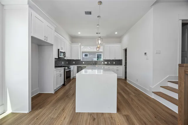 a living room with stainless steel appliances a dining table wooden floor and a view of kitchen