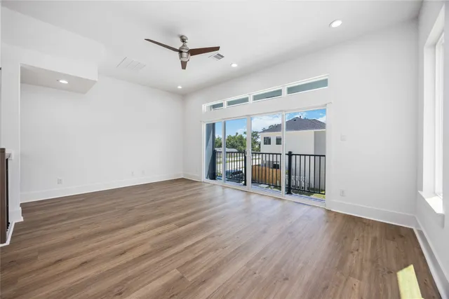 a view of an empty room with wooden floor a ceiling fan and windows