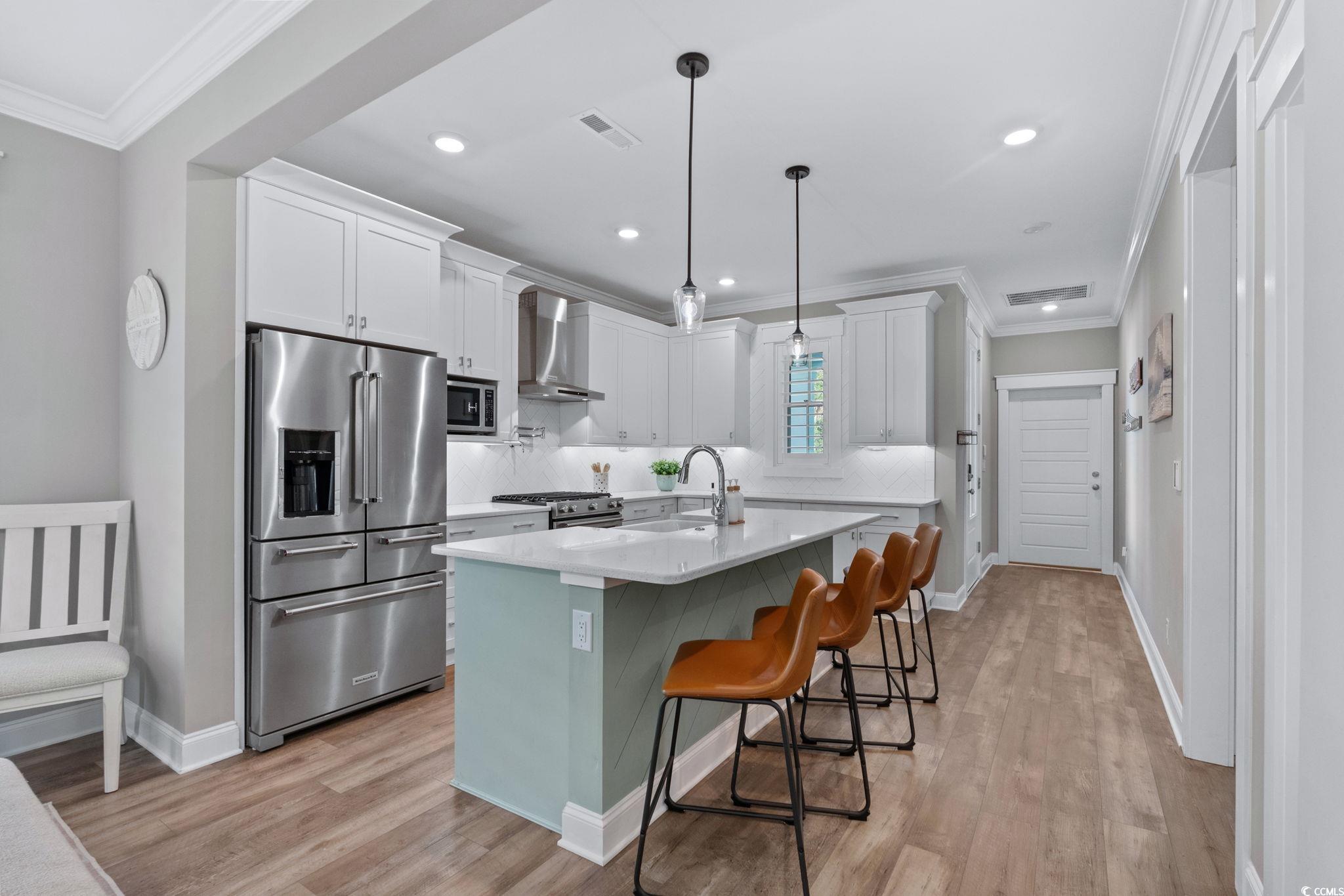 8336 Sandlapper Way Myrtle Beach, SC 29572 - Photo 16 of 40 Kitchen with crown molding, high end appliances, light wood finished floors, a kitchen island with sink, and white cabinets