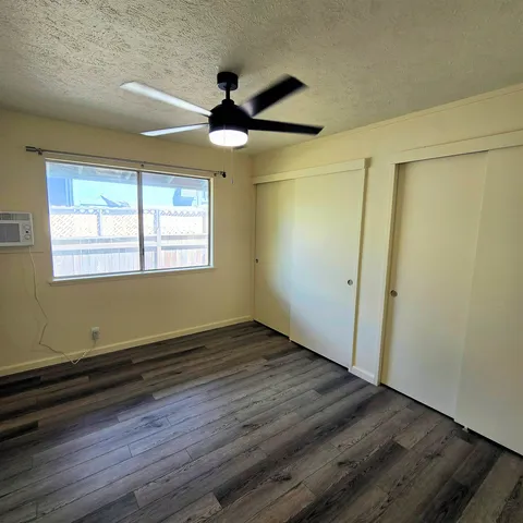 an empty room with wooden floor a ceiling fan and windows