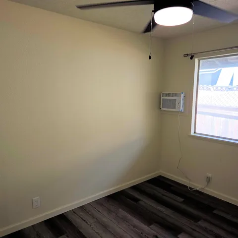 an empty room with wooden floor and a ceiling fan