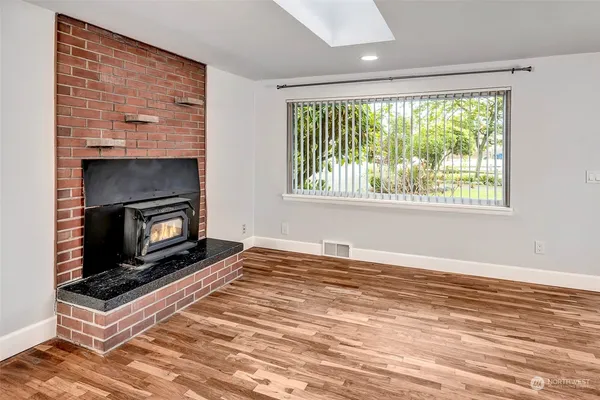 a view of an empty room with wooden floor fireplace and a window