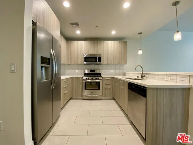 a large kitchen with a large counter top a sink stainless steel appliances and cabinets