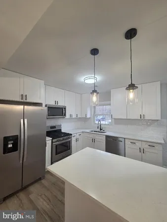 a large white kitchen with a stove a sink dishwasher and a refrigerator with wooden floor