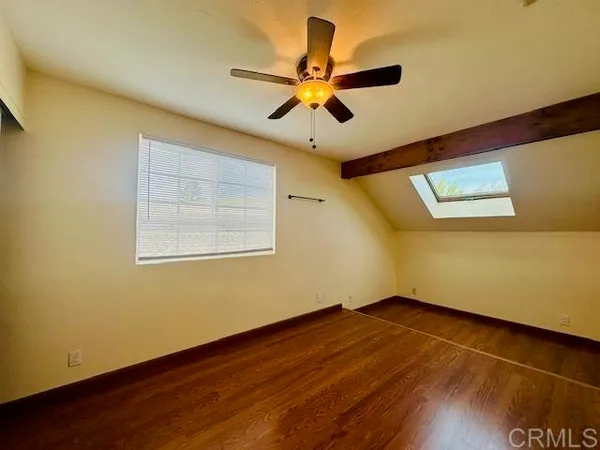 a view of an empty room with wooden floor and a ceiling fan