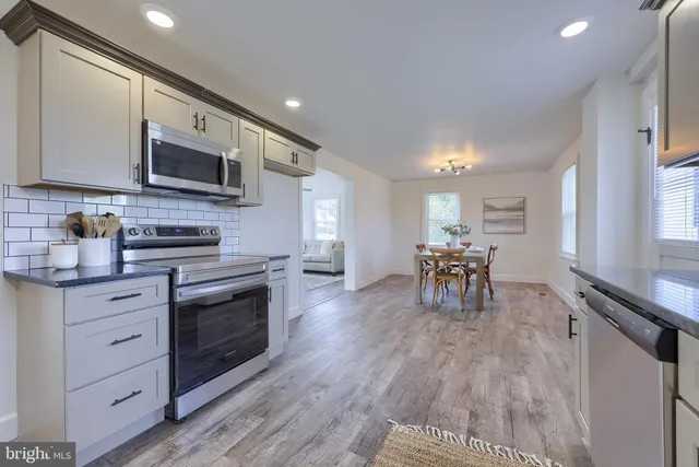 a kitchen with stainless steel appliances granite countertop a stove top oven a sink a dining table and chairs with wooden floor