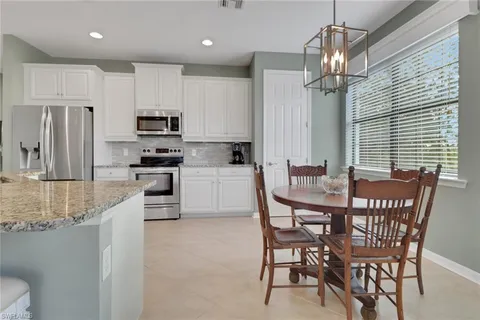 a kitchen with stainless steel appliances kitchen island granite countertop a dining table chairs refrigerator and microwave