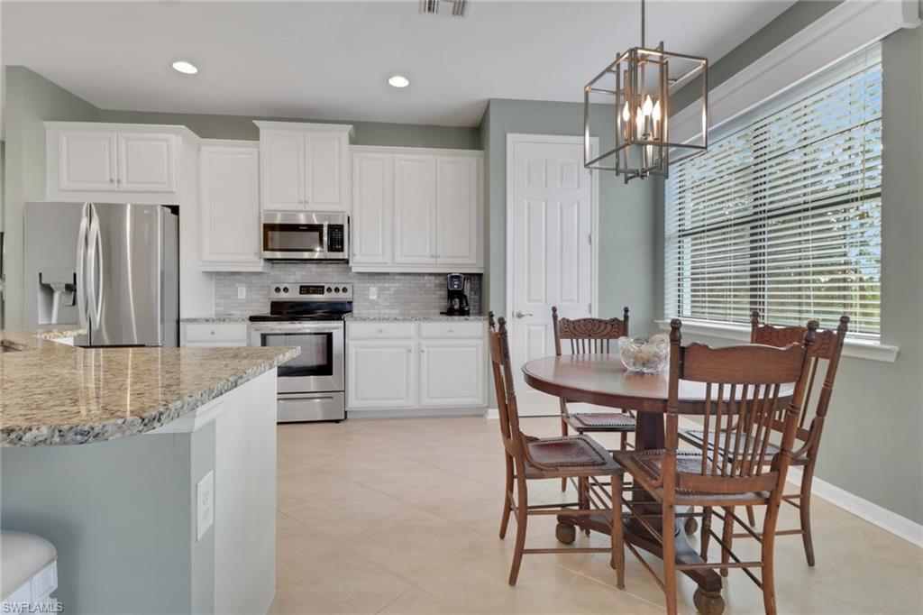26233 Palace Lane, Unit 201 Bonita Springs, FL 34135 - Photo 4 of 46 a kitchen with stainless steel appliances kitchen island granite countertop a dining table chairs refrigerator and microwave
