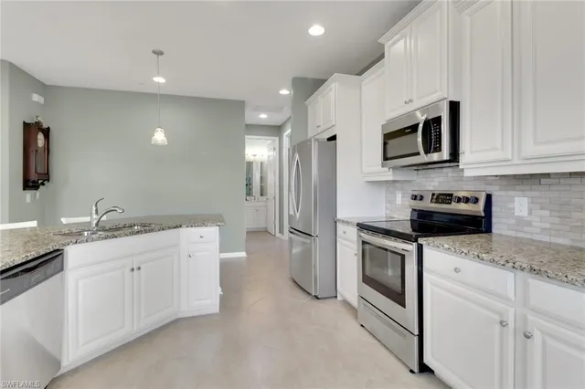 a kitchen with stainless steel appliances granite countertop white cabinets a sink a stove a microwave and a refrigerator