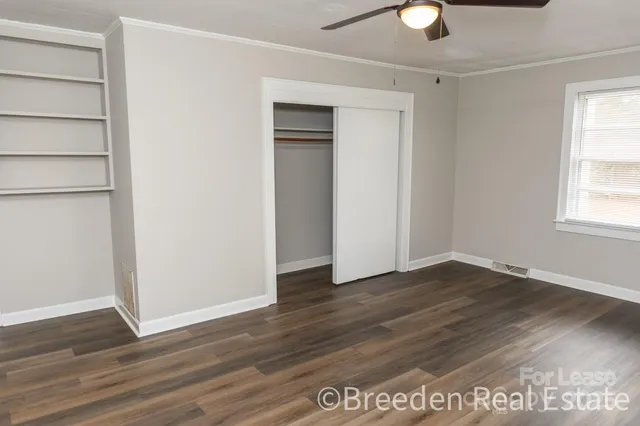 an empty room with wooden floor closet and windows