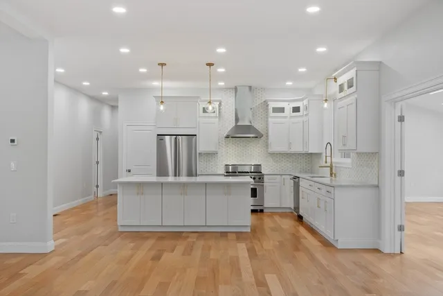 a large kitchen with stainless steel appliances granite countertop a large center island a stove a refrigerator and white cabinets