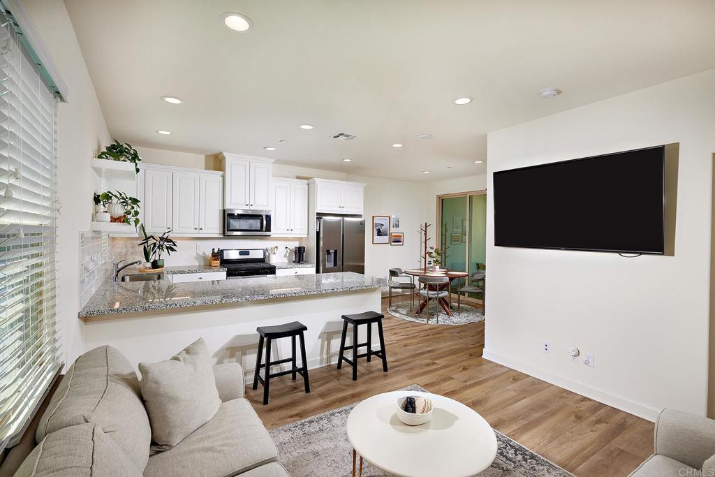 a living room with stainless steel appliances furniture a flat screen tv and kitchen view