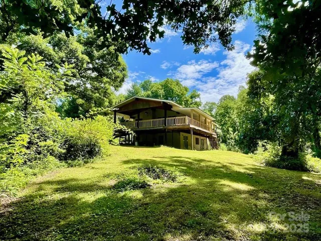 a view of a wooden house with a small yard and large trees