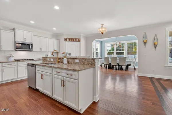 a kitchen with stainless steel appliances a stove a sink a refrigerator and a dining table with wooden floor