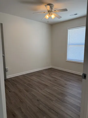 an empty room with wooden floor chandelier fan and windows