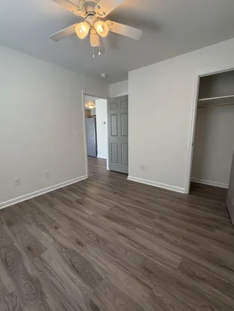 an empty room with wooden floor and way to kitchen