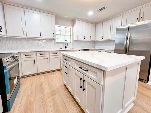 a kitchen with white cabinets appliances a sink and a window