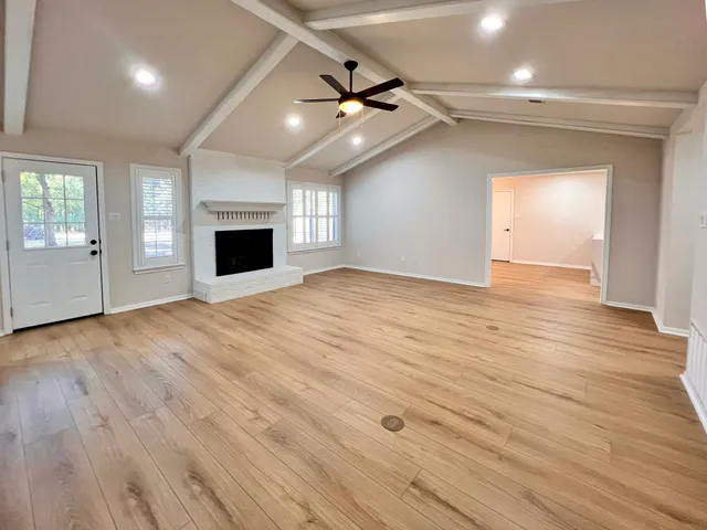 an empty room with wooden floor fireplace and windows