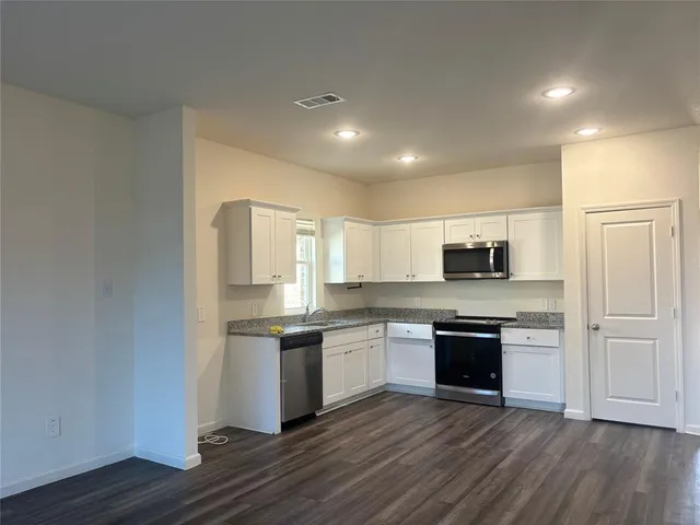 a kitchen with stainless steel appliances granite countertop a stove top oven a sink and white cabinets
