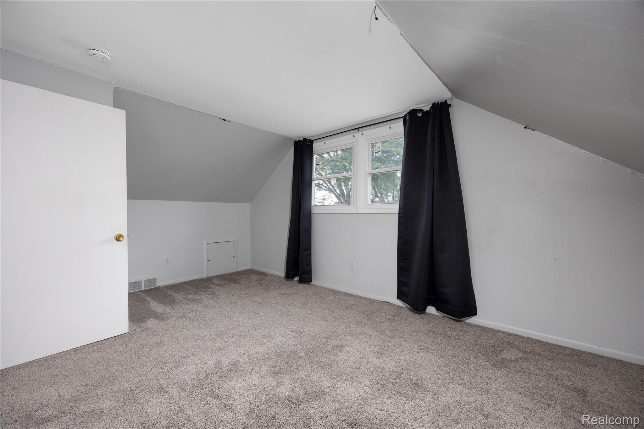 4942 Butler Drive Troy, MI 48085 - Photo 25 of 33 Attic room featuring sloped ceilings, two dormer windows, gray carpeting, a white interior door with a brass-finish knob, and a floor-level access panel