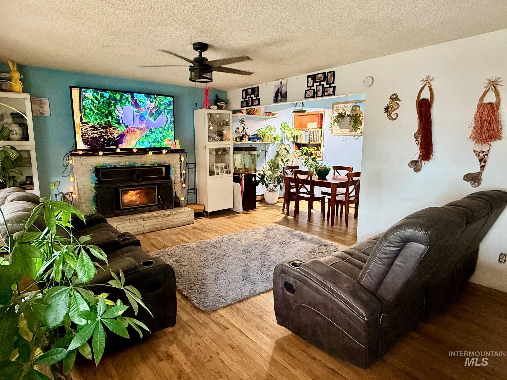 402 Cedar Drive Pierce, ID 83546 - Photo 2 of 24 Living room with hardwood / wood-style floors, a ceiling fan, a lit fireplace, and a textured ceiling