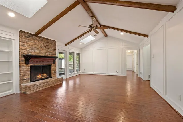 a view of an empty room with wooden floor fireplace and a window