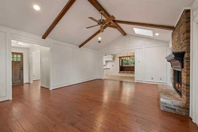 a view of an empty room with wooden floor fireplace and a window