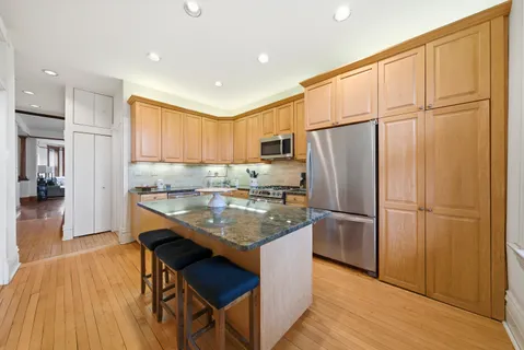 a kitchen with stainless steel appliances granite countertop a refrigerator a sink dishwasher a stove a dining table and chairs with wooden floor