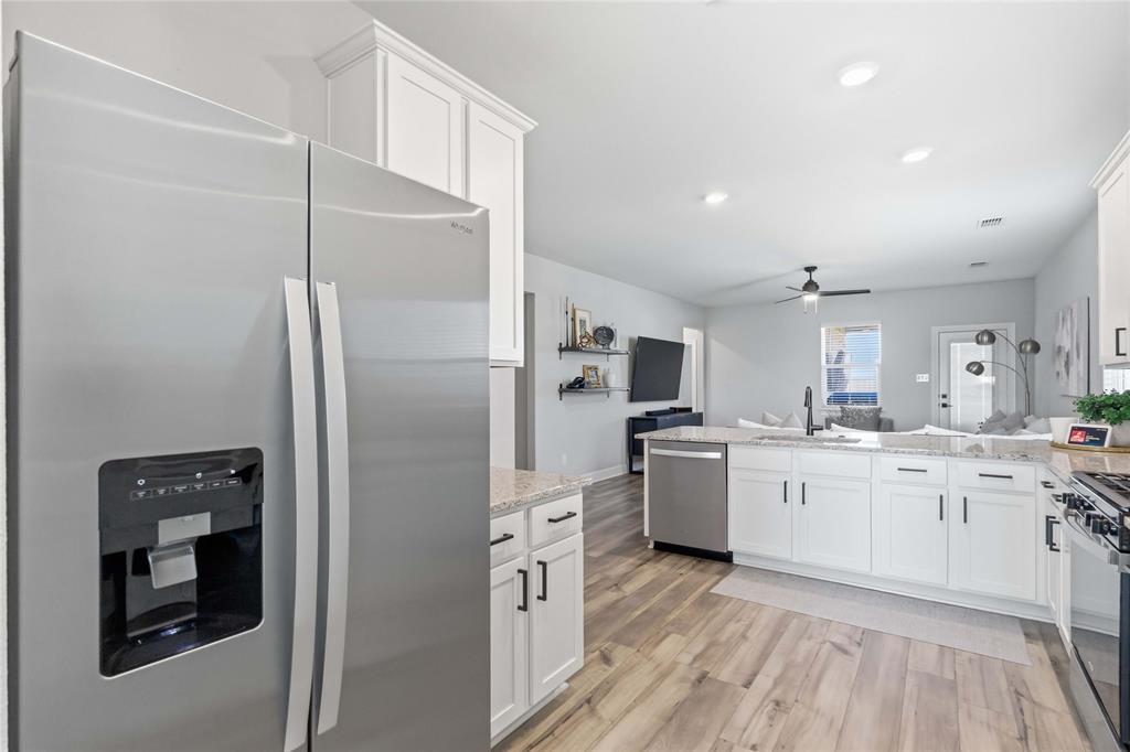 1012 Calhoun Drive Anna, TX 75409 - Photo 12 of 39 Open-concept kitchen featuring wood-finish flooring, white cabinetry with black hardware, stone countertops, and stainless steel appliances