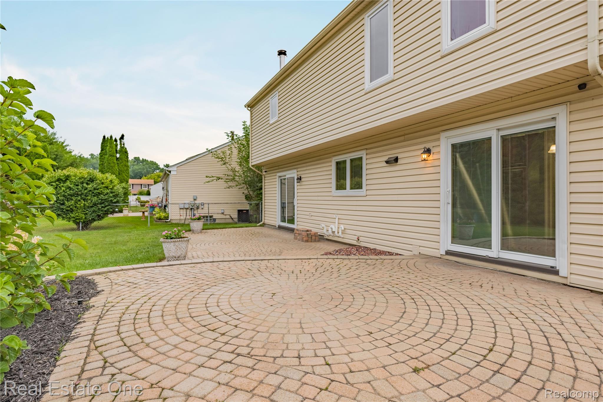 39750 Cheviot Road Canton, MI 48188 - Photo 63 of 71 Expansive paver patio with a circular pattern, featuring two sliding glass doors and exterior lighting