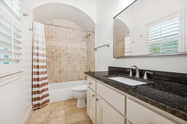 a bathroom with a granite countertop sink a toilet a mirror a bathtub and shower