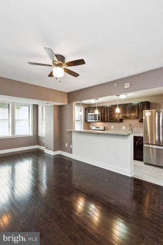 a view of an empty room with kitchen view and wooden floor