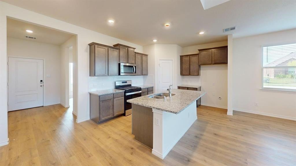 1306 Colonial Bluff Lane Princeton, TX 75407 - Photo 8 of 27 Contemporary kitchen featuring wood-finish flooring, a central island with a double basin sink, stainless steel appliances, granite countertops, and white subway tile backsplash