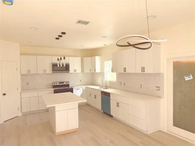 a kitchen with stainless steel appliances a refrigerator a stove a sink and white cabinets