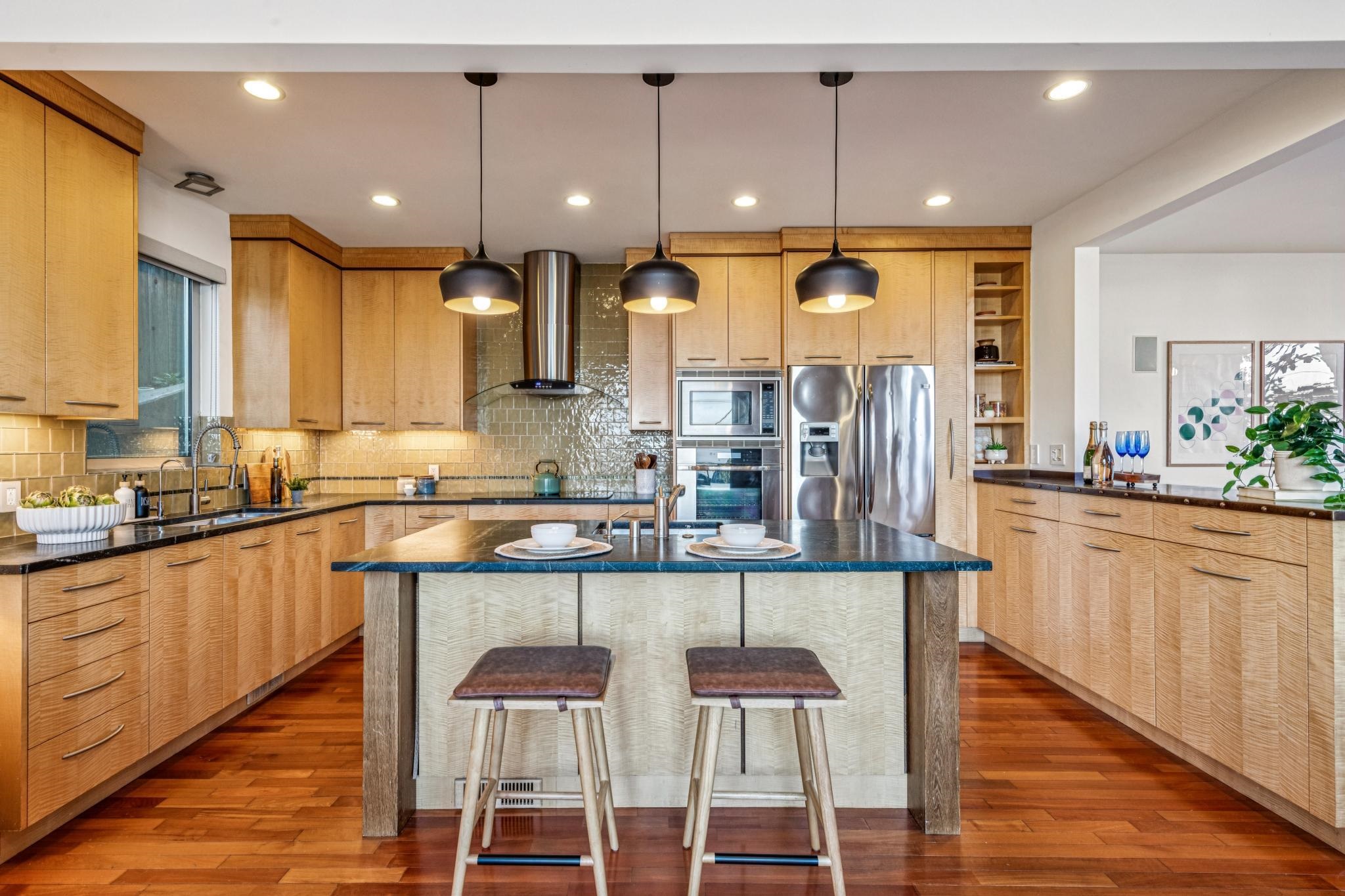 Kitchen featuring a breakfast bar, hanging light fixtures, an island with sink, stainless steel appliances, and tasteful backsplash