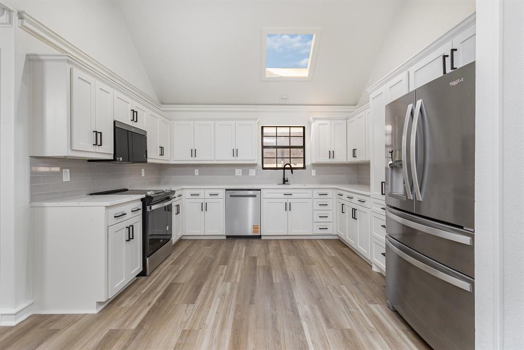 Kitchen featuring vaulted ceiling, stainless steel appliances, white cabinets, light wood-type flooring, and backsplash